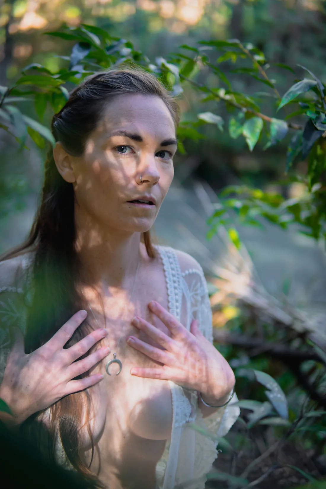 Erin Frances standing in the forest with both hands resting on her heart